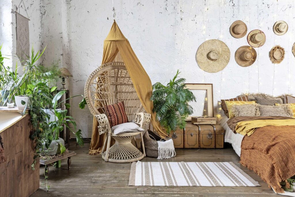 Elegant and quiet bohemian room with cozy interior, wicker chair, pillows, cushions, green plants in flower pot, bed and rug on wooden floor