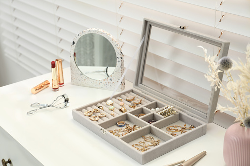 Elegant jewelry box with beautiful bijouterie and makeup products on dressing table indoors